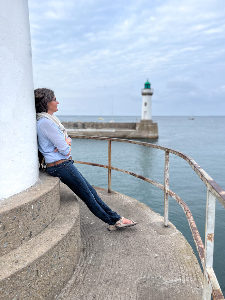 Fotografin aus Flensburg und Glücksburg, Annette Kleinschmidt lehnt an einem Leuchturm und schaut aufs Meer.