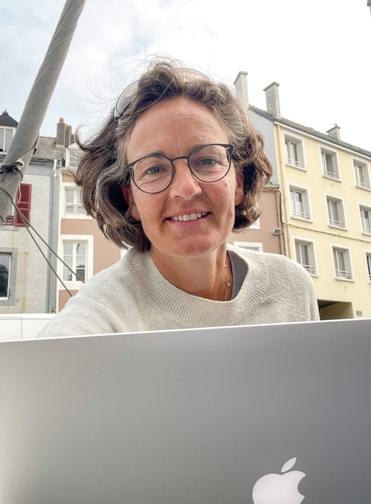 Fotografin in Flensburg am Computer bei der Bildbearbeitung. Annette schaut über ihren Laptop in die Kamera.