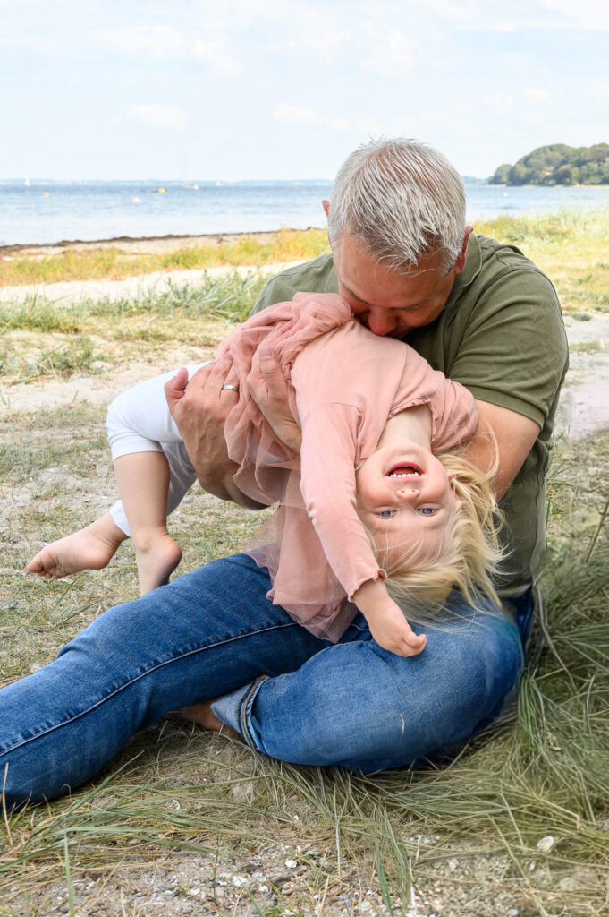 Papa und kleine Tochter machen Quatsch am Strand der Flensburger Foerde