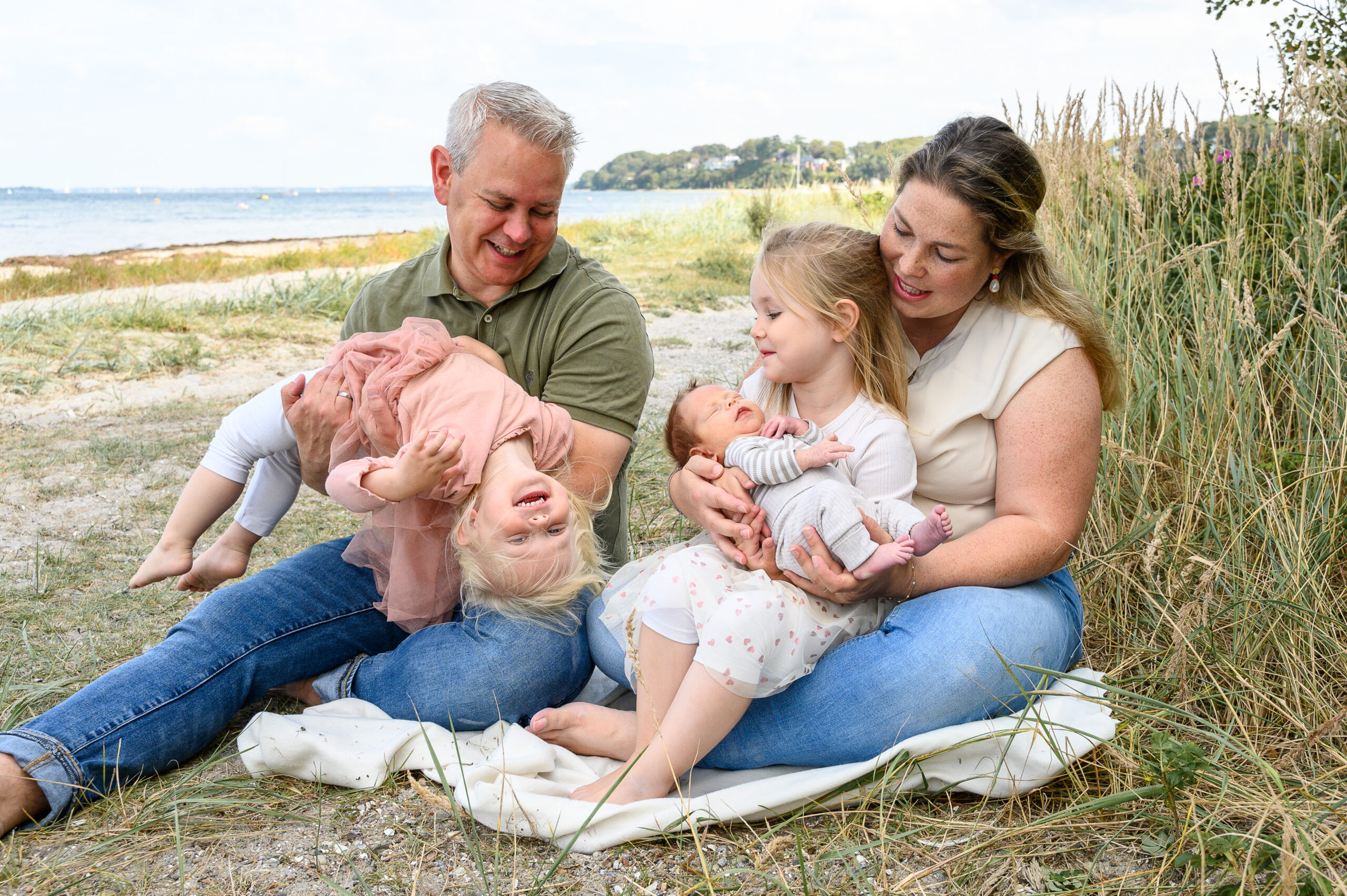 Familie mit drei kleinen Kindern sitzen froehlich ungestellt am Strand in Gluecksburg für ein natürliches Familienfoto