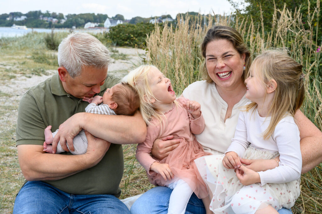 Familie sitzt am Gluecksburger Strand in Quellental und Mama lacht froehlich in die Kamera der Fotografin
