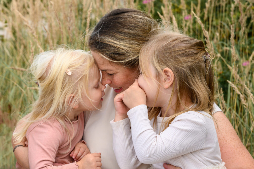 Mutter hat ihre Töchter eng auf dem Schoss in der Natur und kuschelt mit ihren Kindern