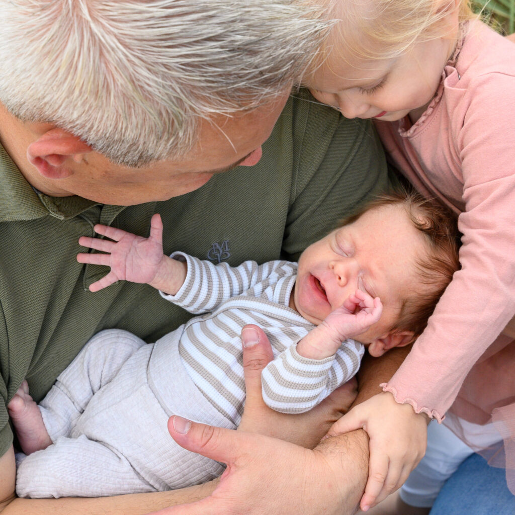 das Neugeborene liegt im Arm vom Vater und der grossen Schwester