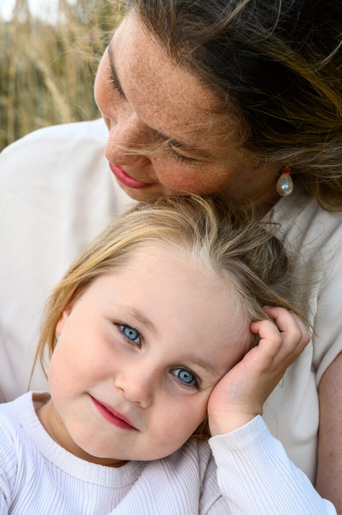 Mama hat die grosse Tochter auf dem Schoss in der Natur und das Maedchen guckt zur Fotokamera