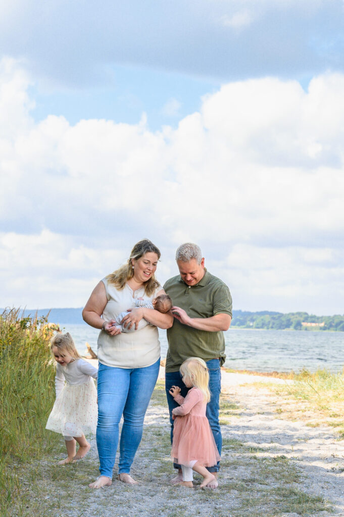 Familie stehend am Strand an der Flensburger Förde die Toechter laufen fröhlich in ihren Sommerkleidchen um die Eltern herum