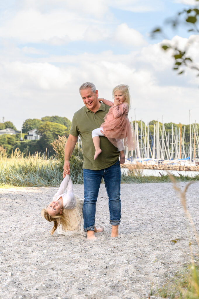 Vater steht am Strand vor dem Flensburger Segel Club FSC und hat Spass mit seinen Kindern