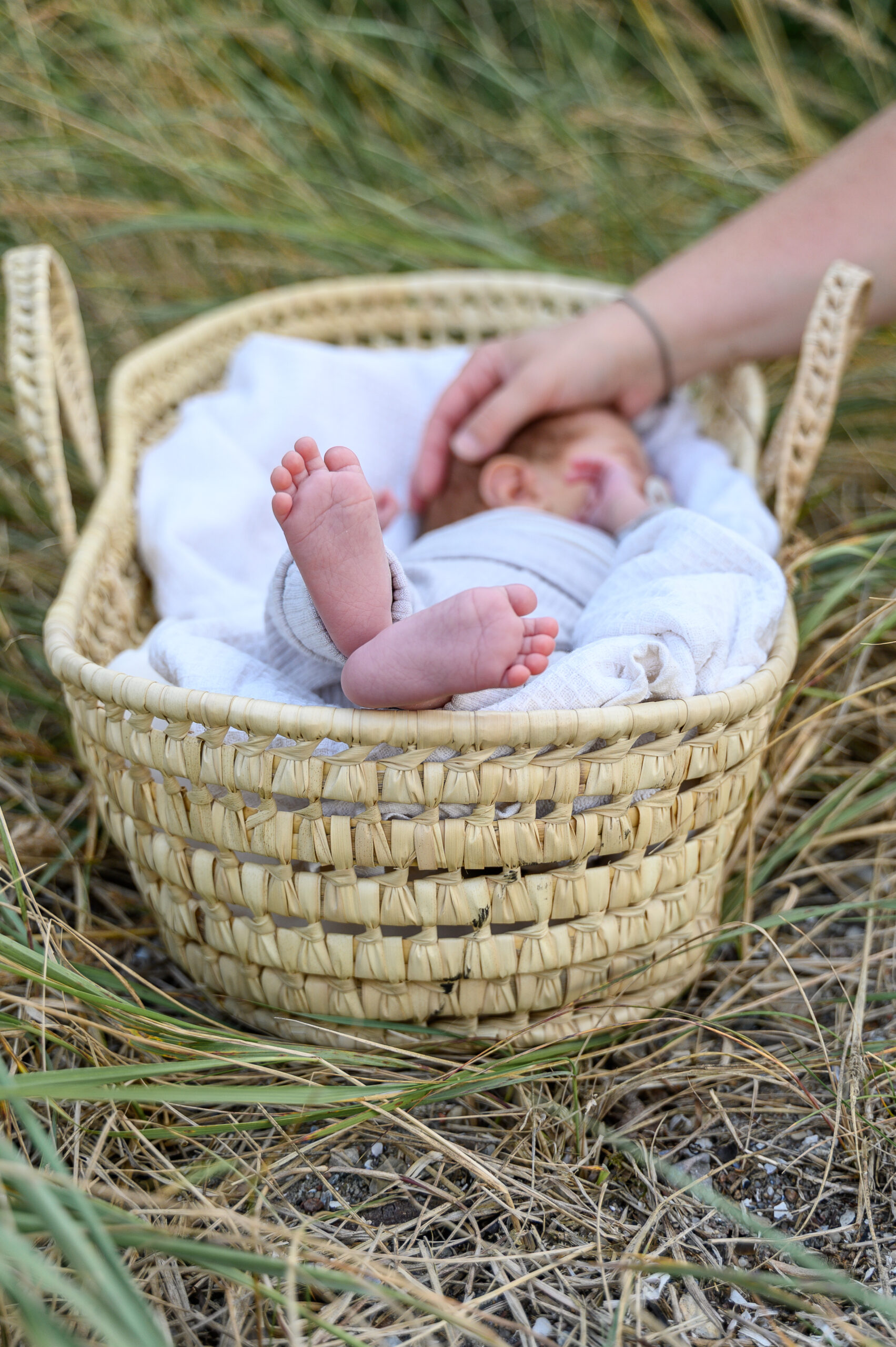 baby liegt in einem Korb am Strand in Gluecksburg mit nackten Babyfuessen während die Hand der Mutter den Kopf des Neugeborenen streichelt