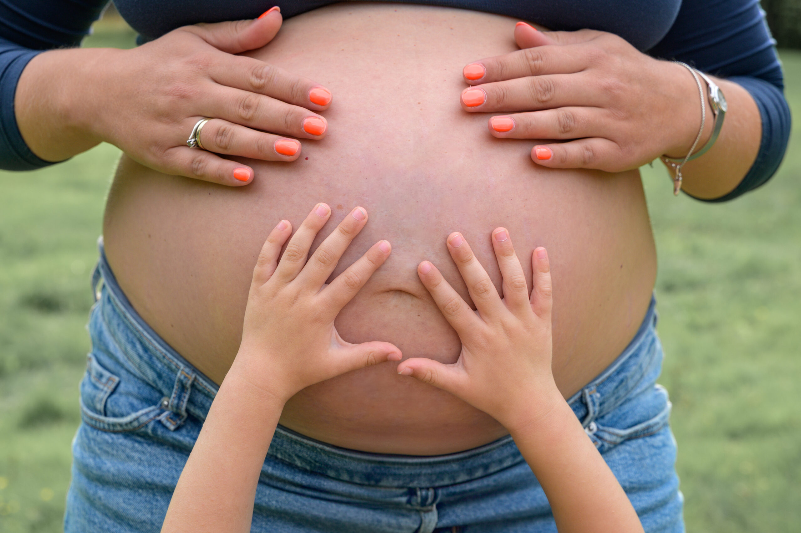 Mamas Haende und Kinder Haende liegen auf dem schwangeren Bauch und fühlen das Baby in der Natur