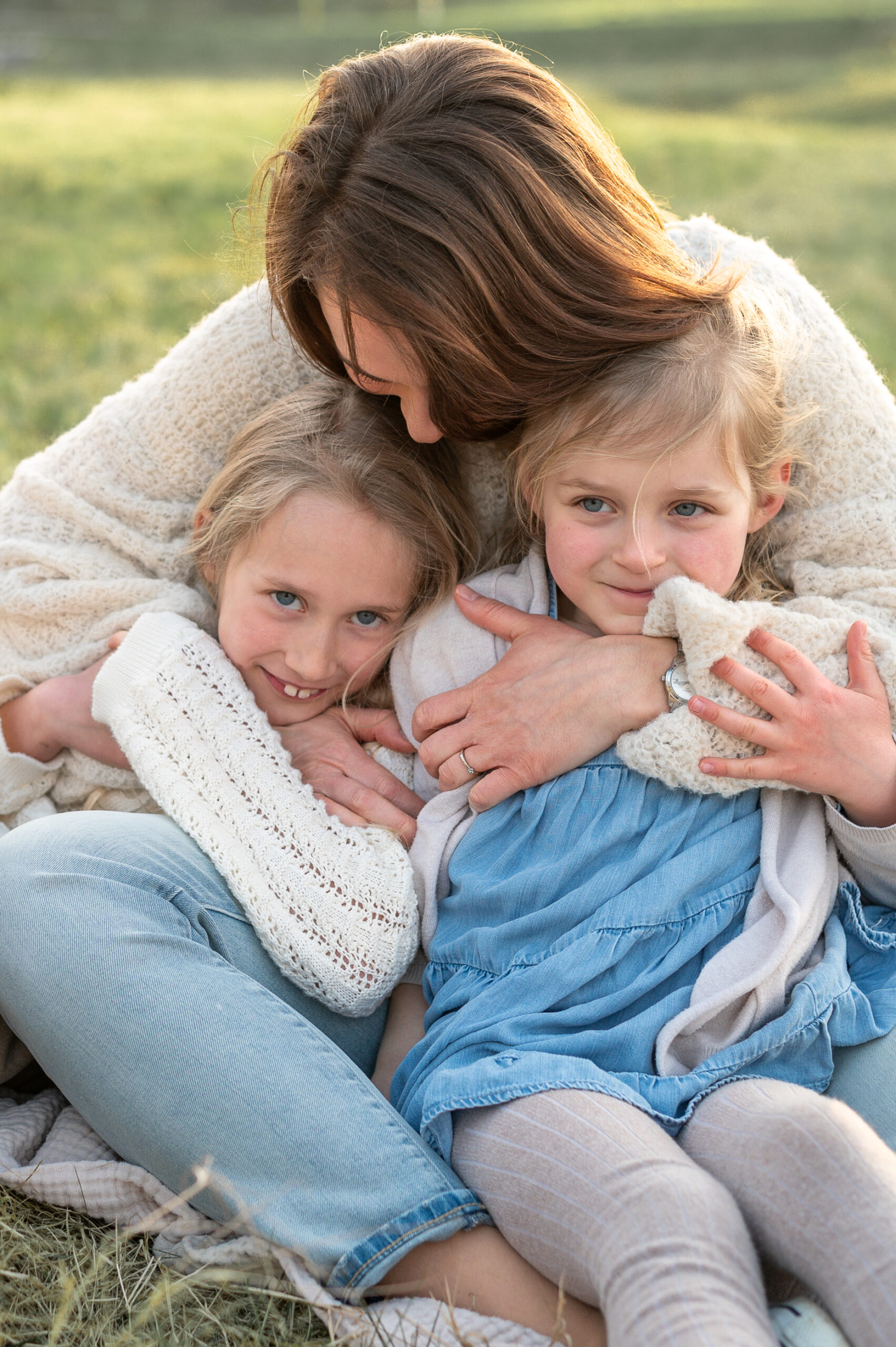 Mutter und Toechter sitzen kuschelnd auf einer Decke in der Natur in Flensburg und halten sich eng umschlungen im Arm