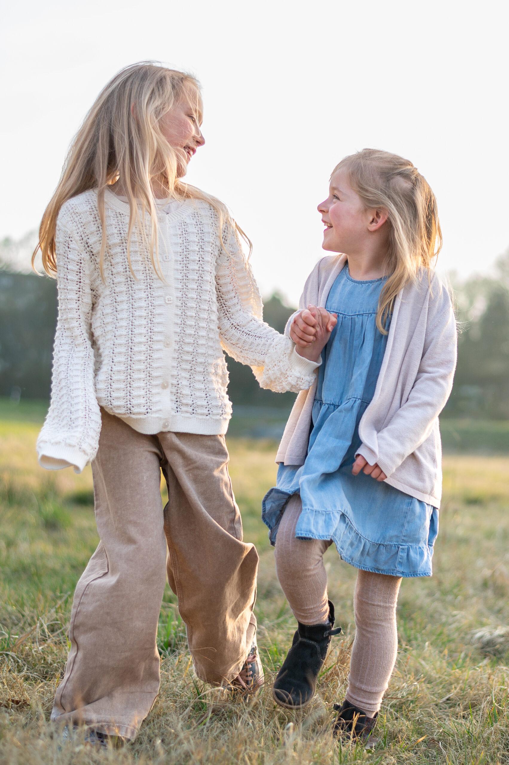 zwei Schwestern gehen Hand in Hand über eine Wiese in Flensburg und schauen sich froehlich an