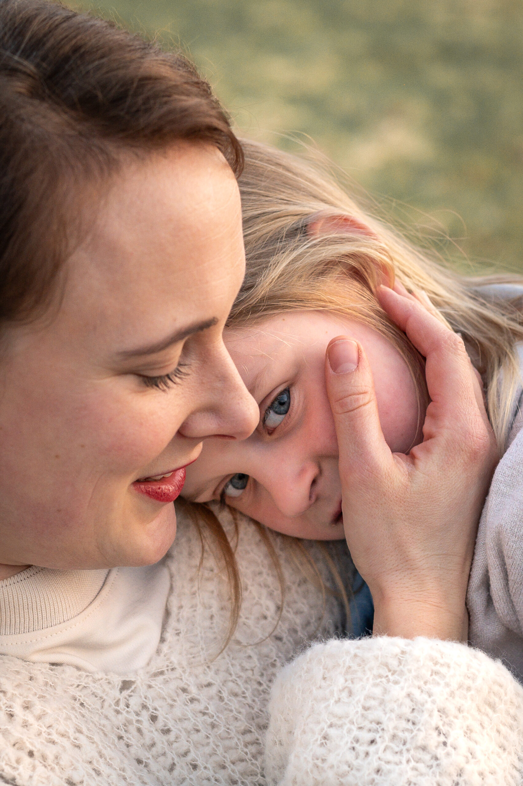 Tochter legt ihren Kopf auf die Schulter ihrer Mutter, die die Wange ihrer Tochter hält und liebevoll zu ihr guckt