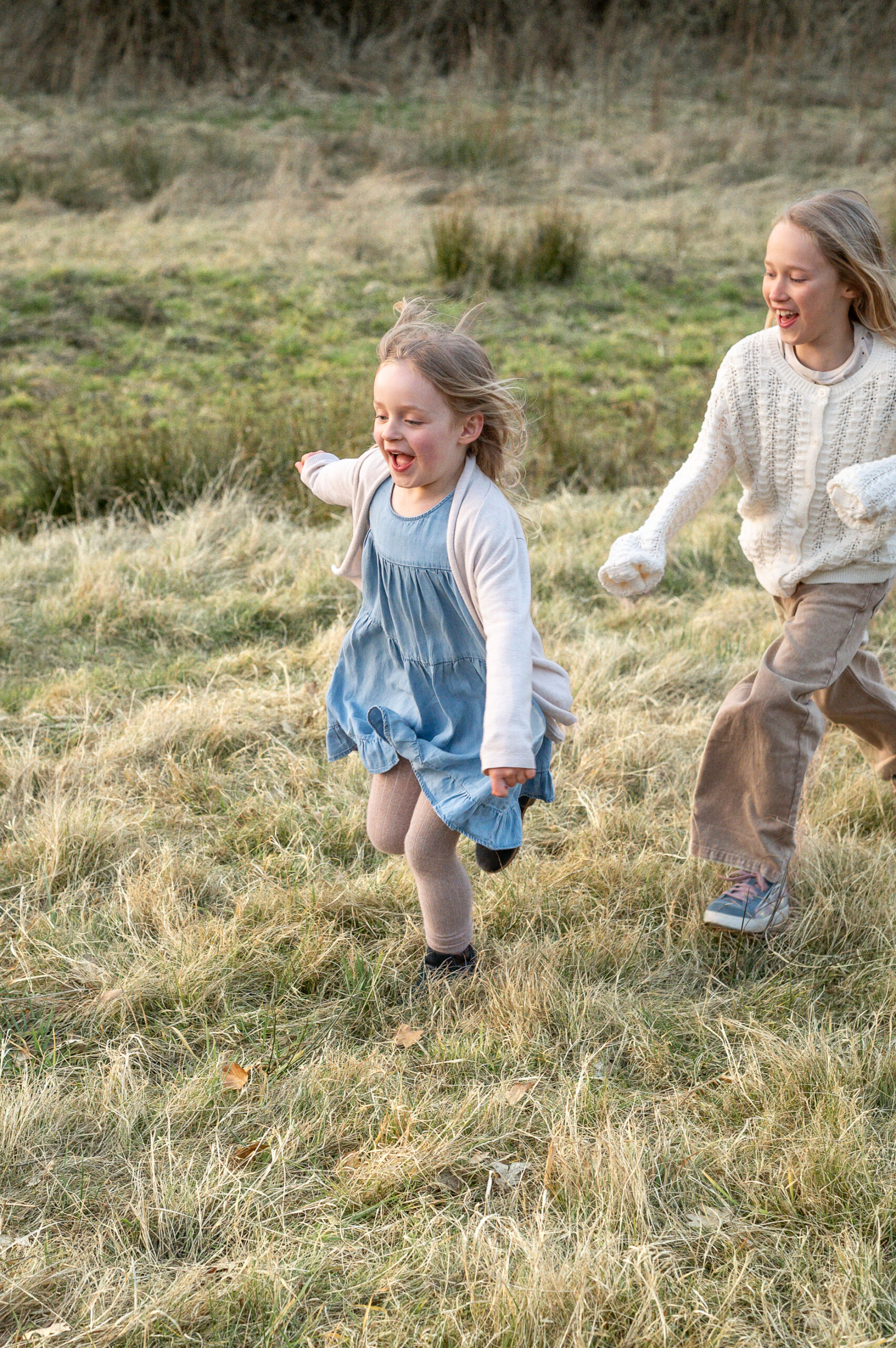zwei Schwestern rennen ausgelassen ueber ein Wiese in der Natur