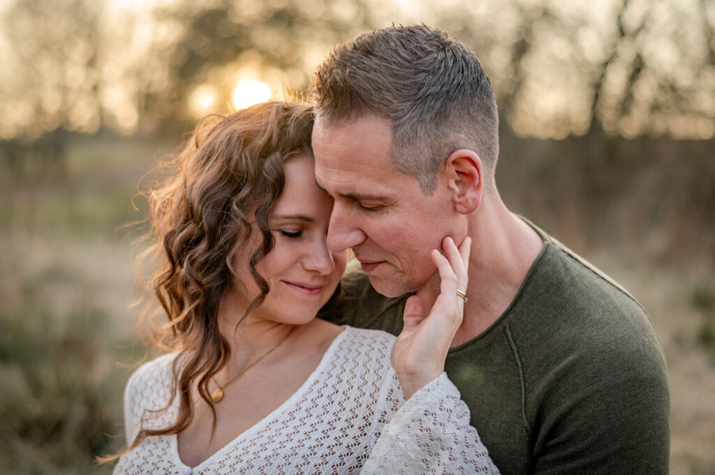 werdende Eltern halten ihre Koepfe nah aneinander und geniessen mit geschlossenen Augen in der Natur in Flensburg