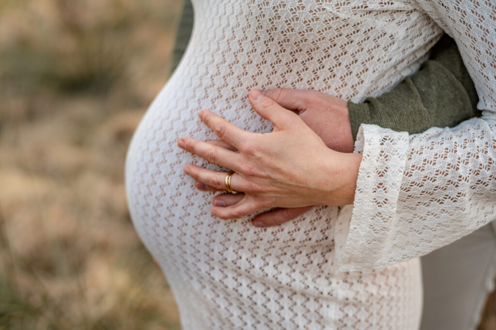 bekleideter Babybauch beim Shooting und die Haende der werdenden Eltern auf dem Bauch.