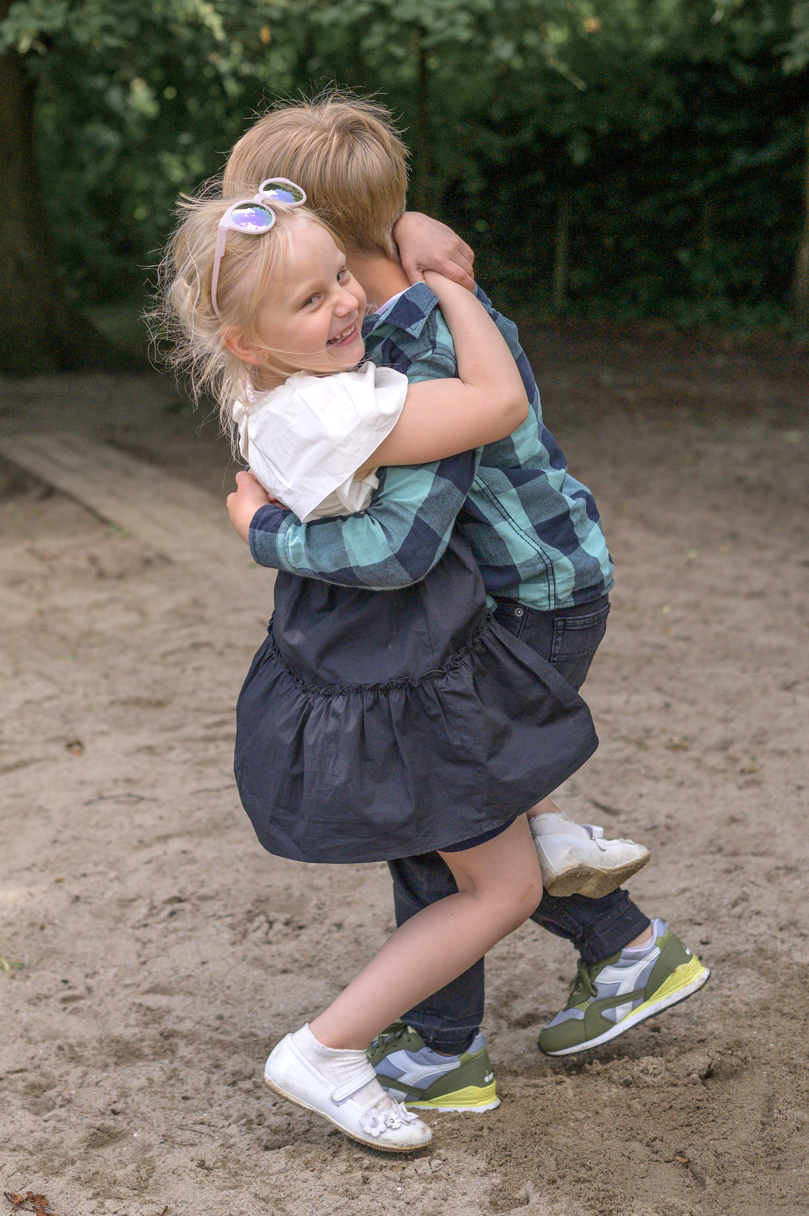 Kindergarten Geschwisterkinder machen Quatsch am Fototag in der Kita. Bruder und Schwester umarmen sich und fallen dabei fast in den Sand.