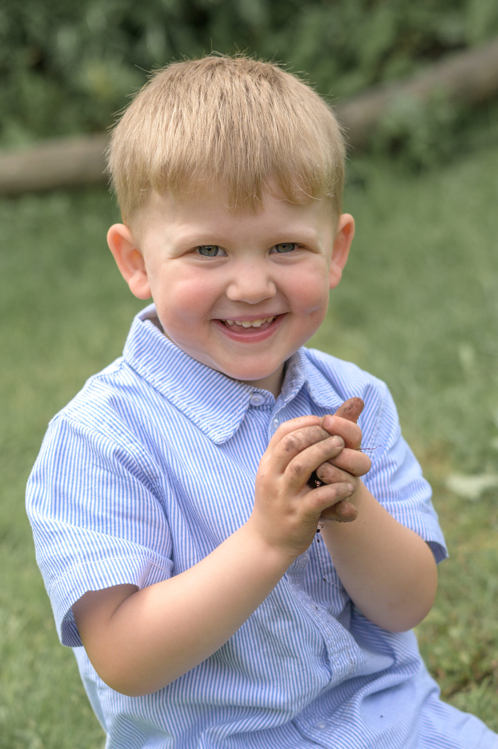 Kita Junge lachend mit dreckigen Händen auf der Wiese während der natürlichen Kindergarten Fotografie in Flensburg