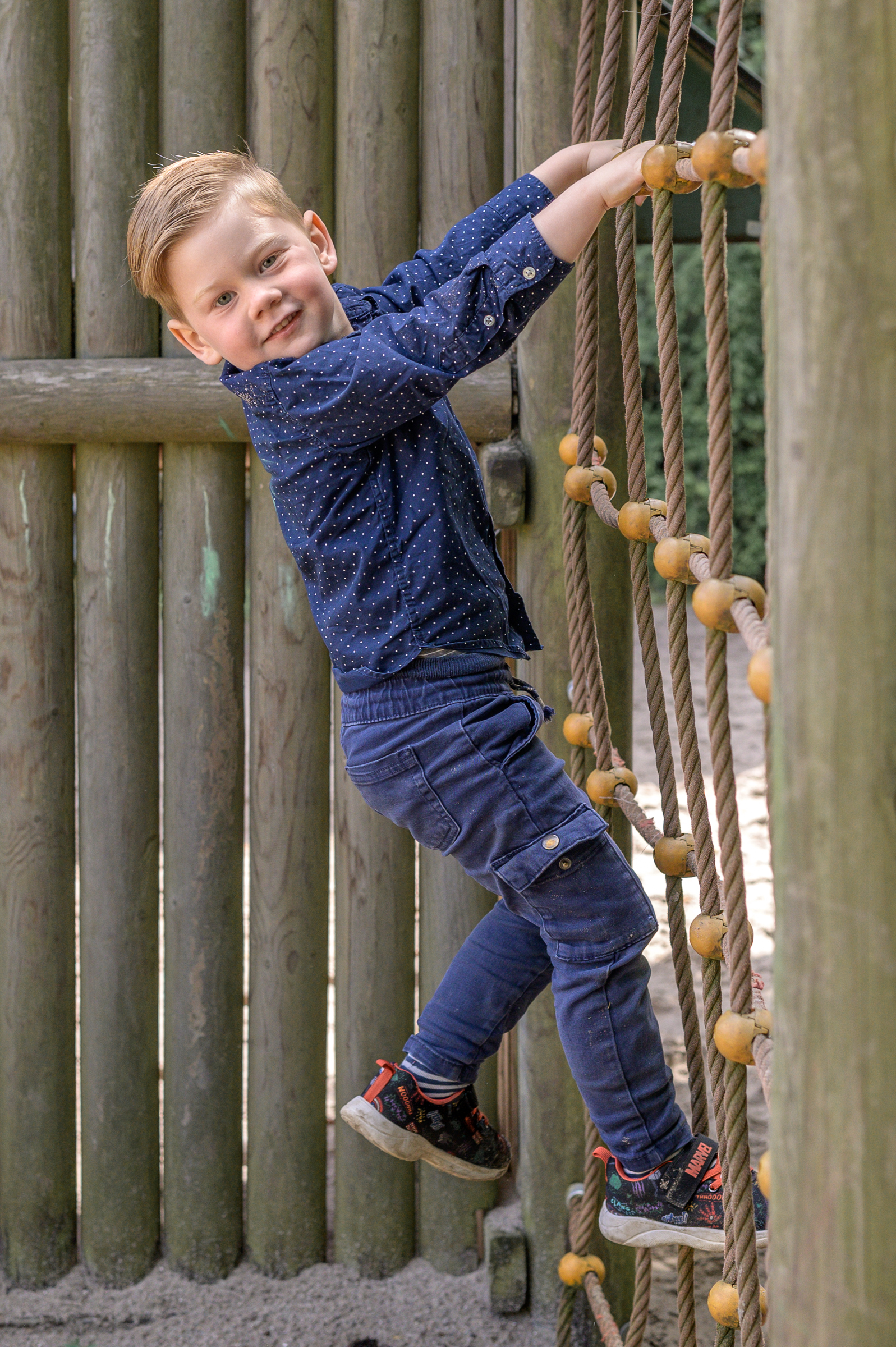 Junge im Kindergartenalter klettert auf dem Spielplatz der Kita und zeigt der Fotografin, wie viel Spass es ihm bringt.