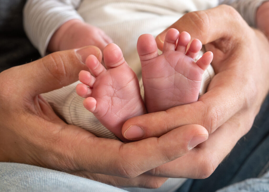 kleine Babyfuesse in den grossen Händen des Vaters. Eine Detailaufnahme beim Newbornshooting zu Hause in Gluecksburg.