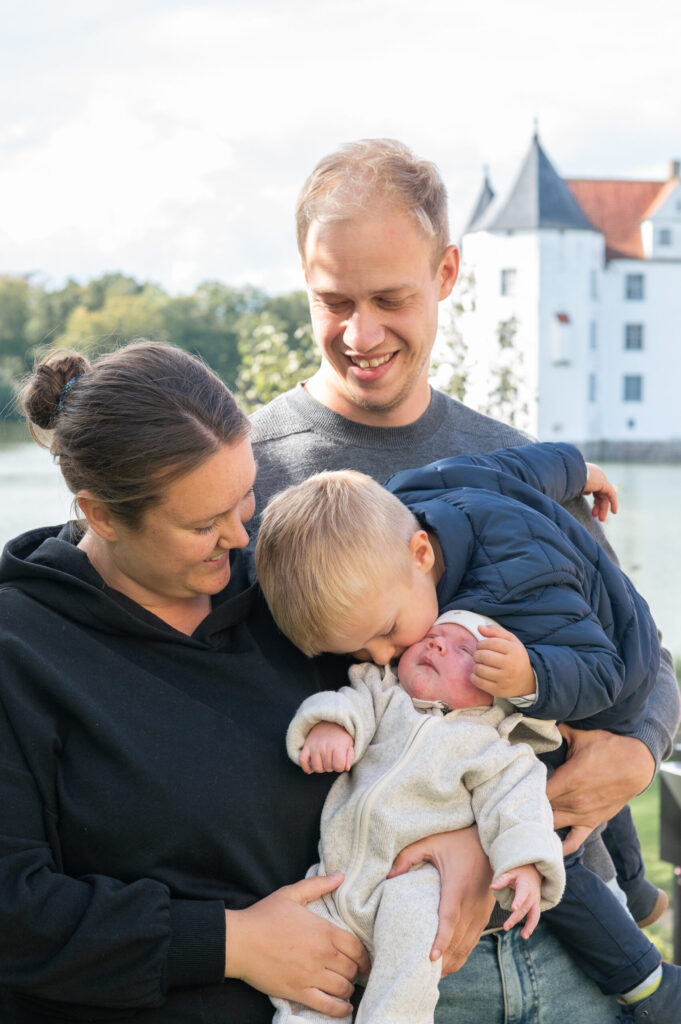 Familienfoto mit Mutter, Vater, und zwei Kindern vor dem Glücksburger Schloss. Der große Bruder gibt seinem Babybruder einen Kuss.